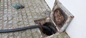 Caixa de gordura aberta durante manutenção, com mangueira de sucção posicionada dentro da caixa