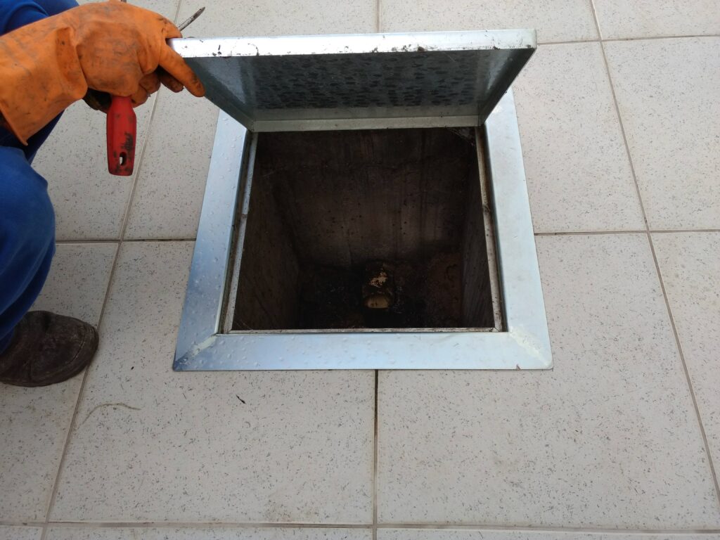 Tampa metálica de caixa de inspeção aberta no piso, com o interior da caixa à mostra