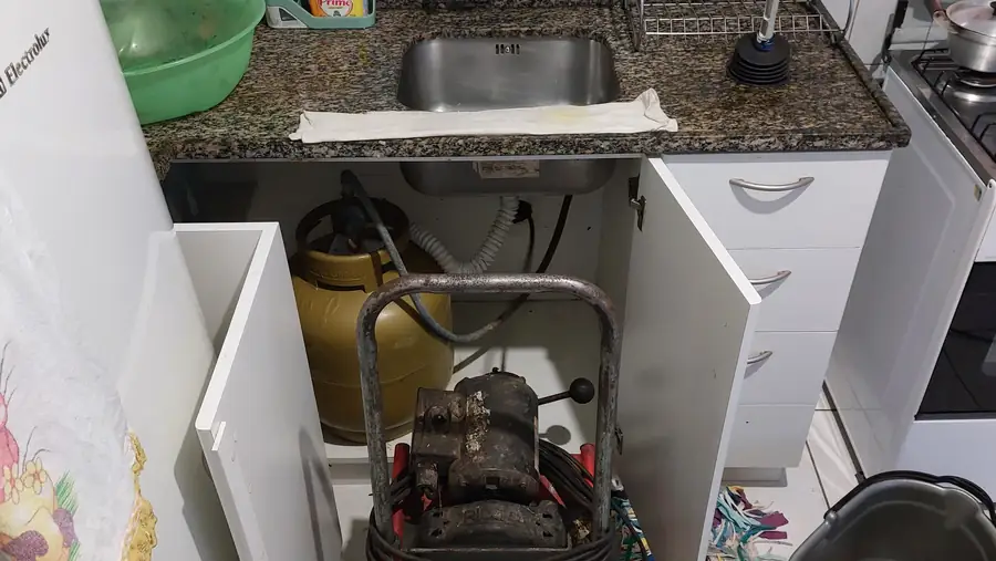 Máquina desentupidora sendo usada para limpar o ralo da pia da cozinha em residência de Curitiba